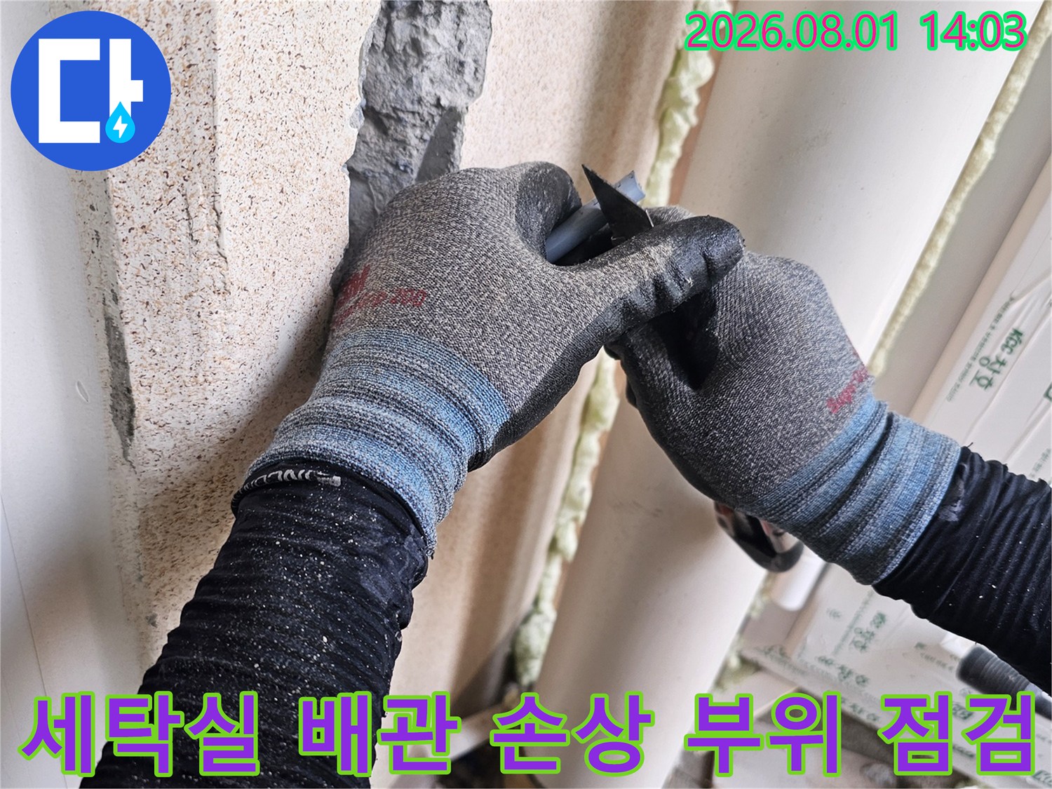 장갑 낀 작업자가 세탁실 타일 파손부 내의 배관을 확인하는 모습