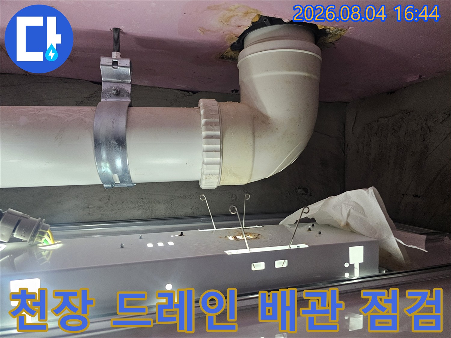 어두운 천장 내부에 위치한 하얀색 파이프와 연결 소켓을 정밀하게 관찰하는 모습