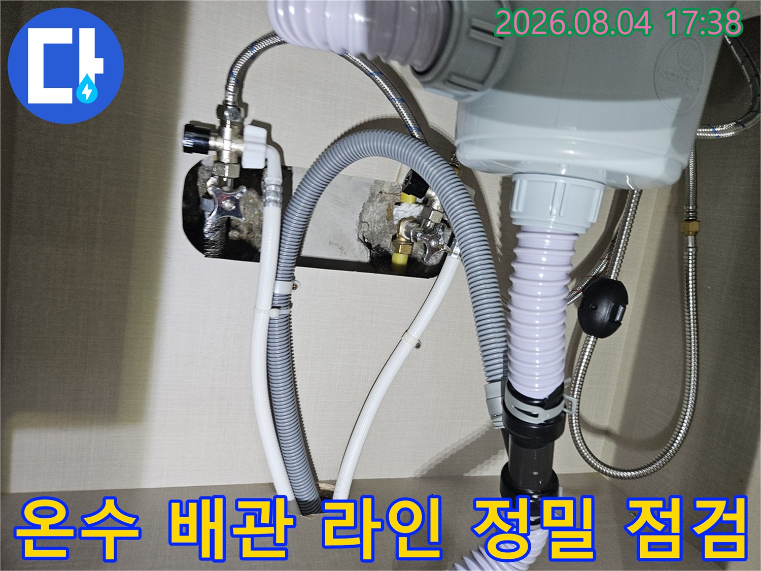 주방 싱크대 아래의 회색 주름관과 스테인리스 소재의 수도 밸브와 연결부
