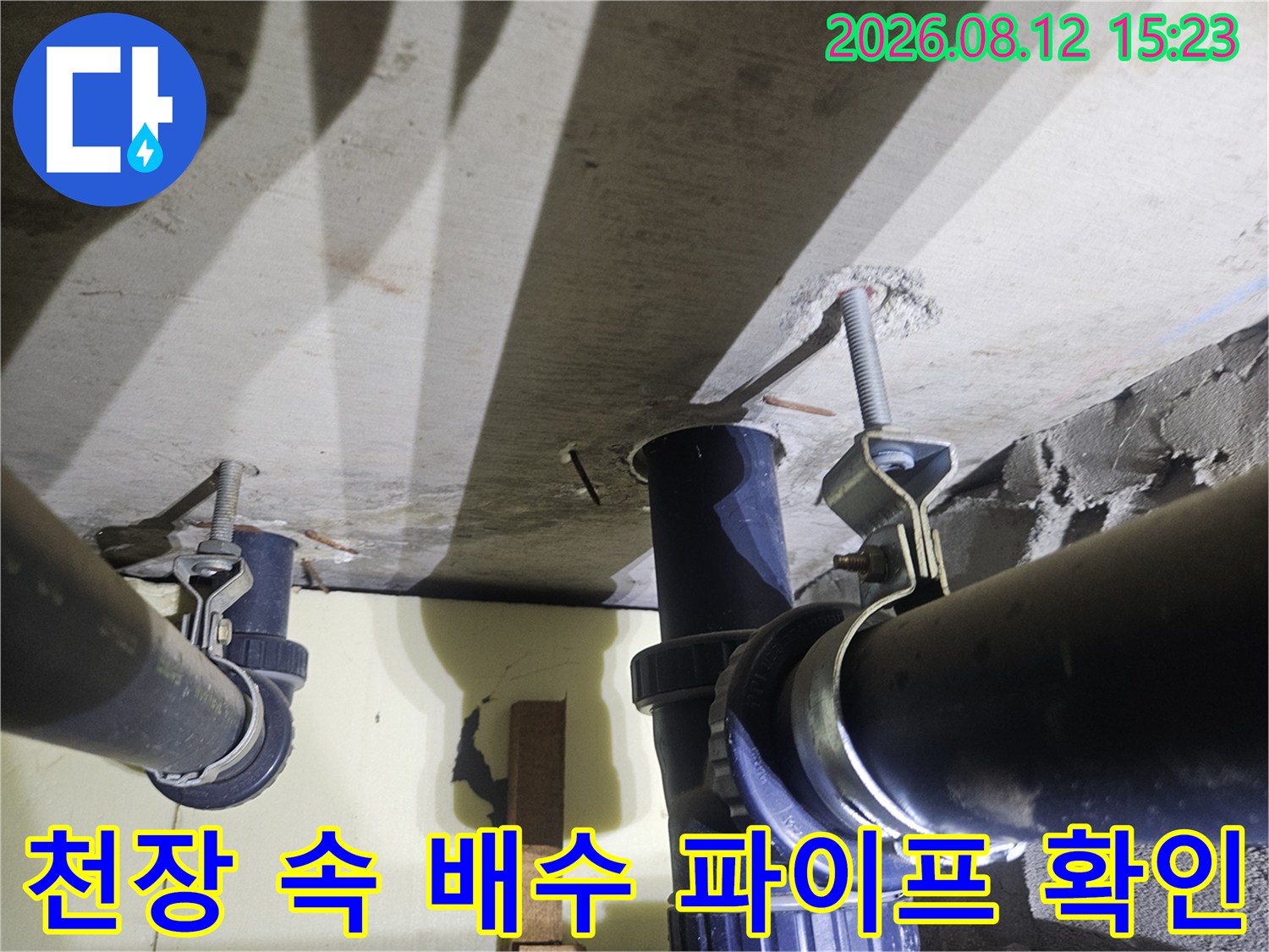 천장 콘크리트 면에 고정된 검은색 플라스틱 하수관과 금속 행거 사진