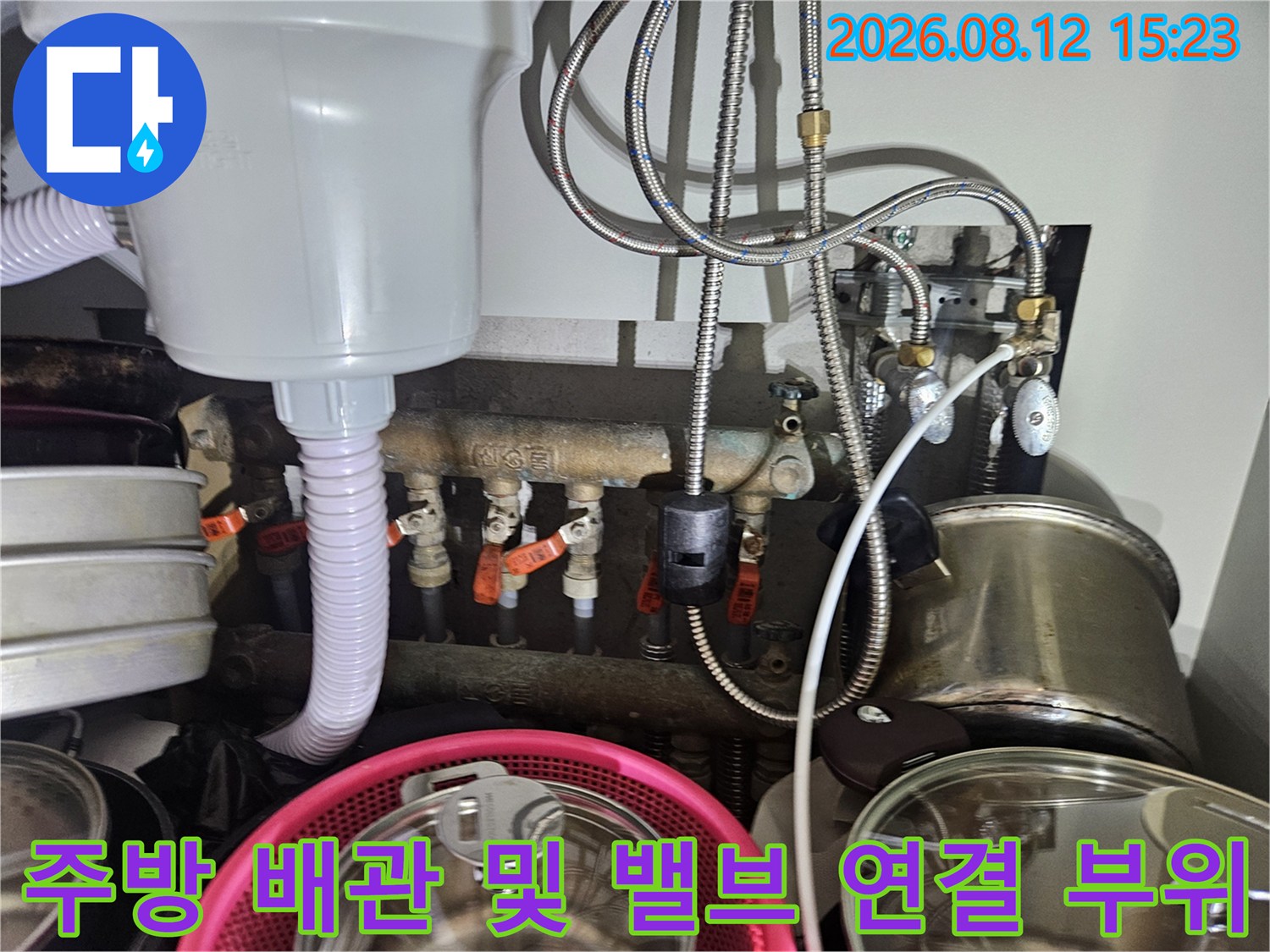 흰색 필터 케이스와 금속 소재의 유연한 급수 호스들이 복잡하게 배치된 주방 하부 구조