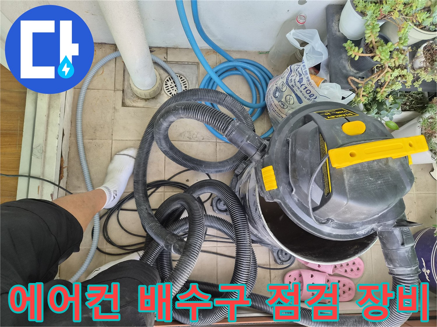 베란다 바닥 배수구 근처에 놓인 산업용 청소기와 배관 연결 호스