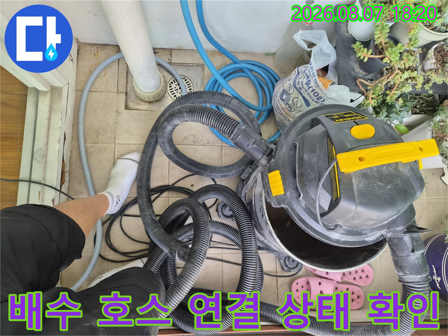 에어컨 배수용 파란색 호스와 현장 작업 장비가 놓인 베란다 모습입니다.