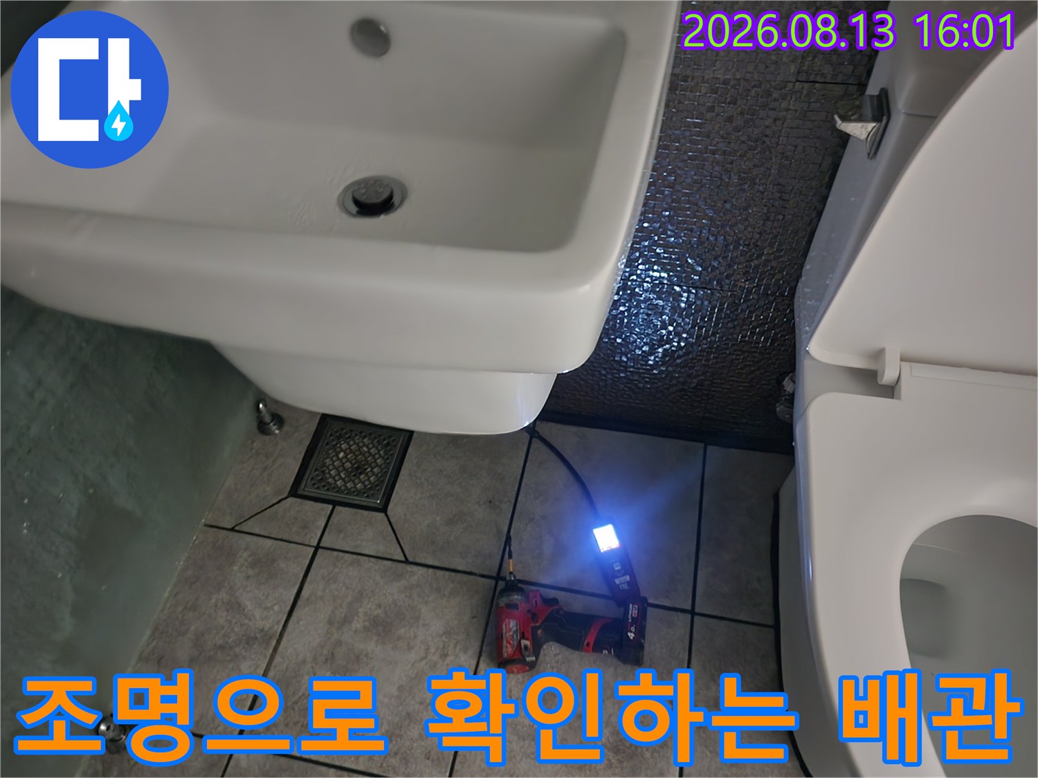 작업용 라이트를 사용하여 세면대 밑 배관 상태를 비추고 있습니다.