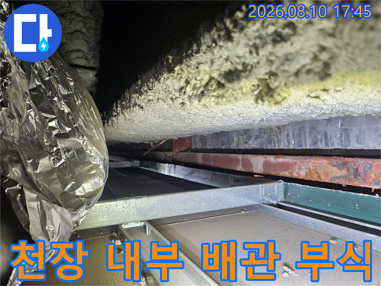 습기에 노출된 천장 배관 보온재와 녹슨 금속 구조물의 모습입니다.
