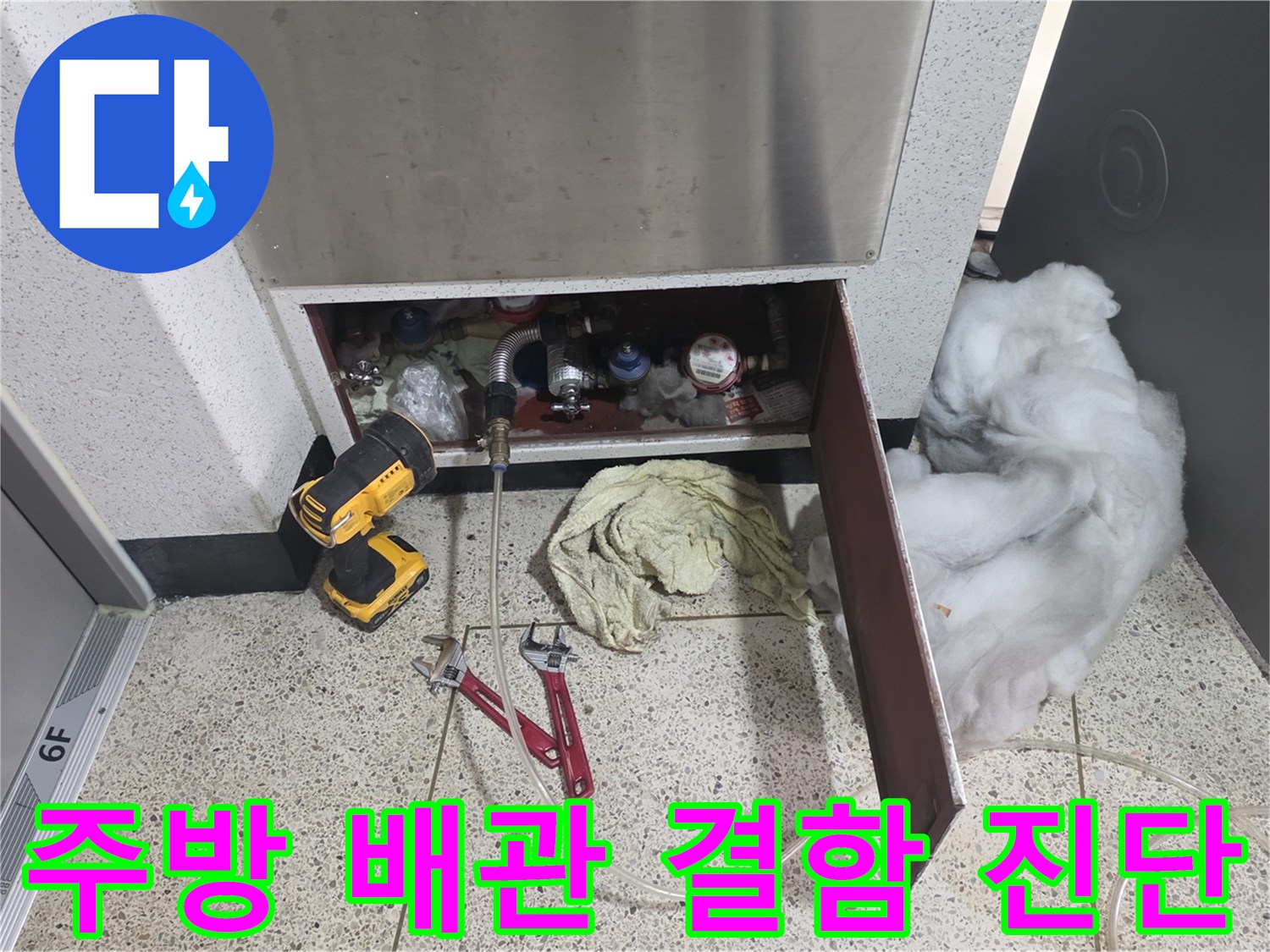 싱크대 하단부의 복잡한 배관들과 그 앞에 놓인 작업 도구들의 모습