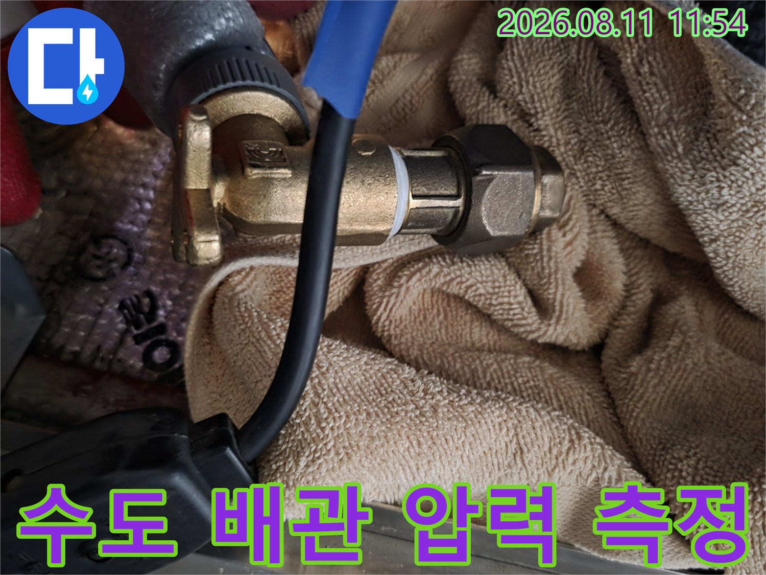 황동 소재의 배관 연결 부위에 정밀 장비를 설치하여 점검하는 장면입니다.