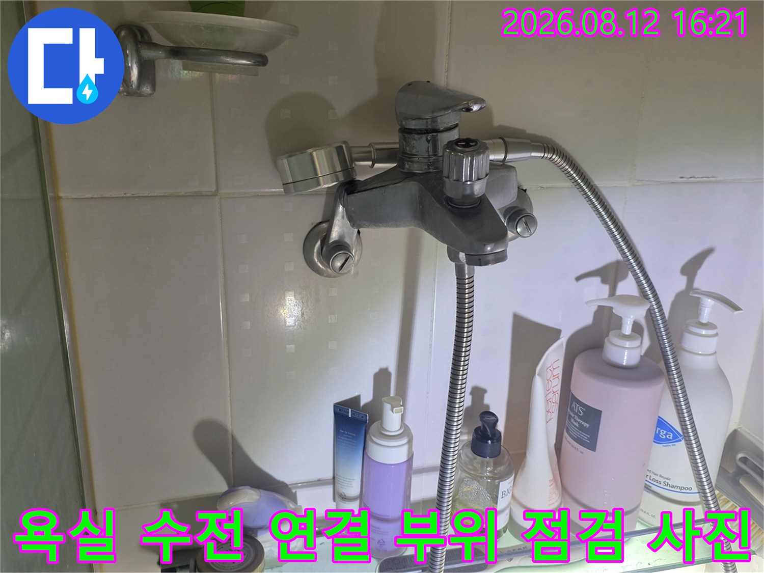 흰색 타일 벽면에 설치된 은색 욕실 수전과 샤워 호스-연결 부위 상태 확인 모습