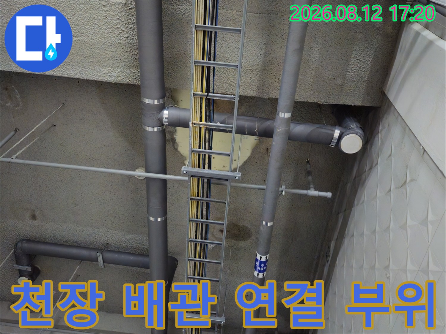 지하주차장 천장에 설치된 회색 배수 파이프와 전기 트레이 시설물입니다.