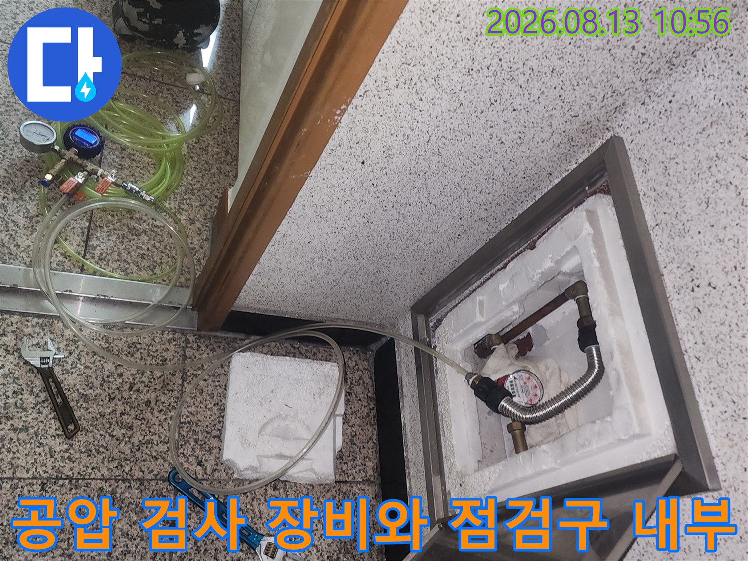 열려 있는 바닥 점검구 안쪽 배관에 압력 측정기가 연결되어 있고 주변에 공구가 배치된 사진