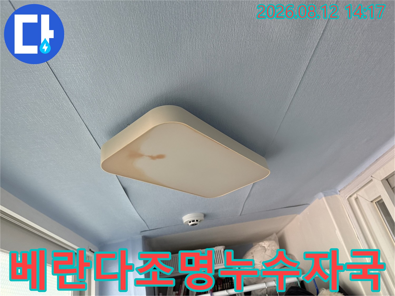 하늘색 천장에 부착된 사각 조명 덮개에 갈색의 누수 얼룩이 생긴 사진