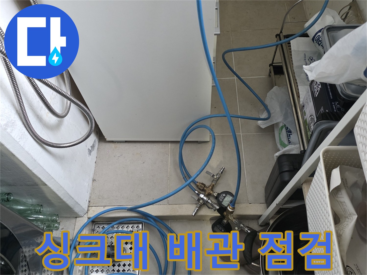 파란색 호스가 얽혀 있는 싱크대 하부 배수 시스템의 모습