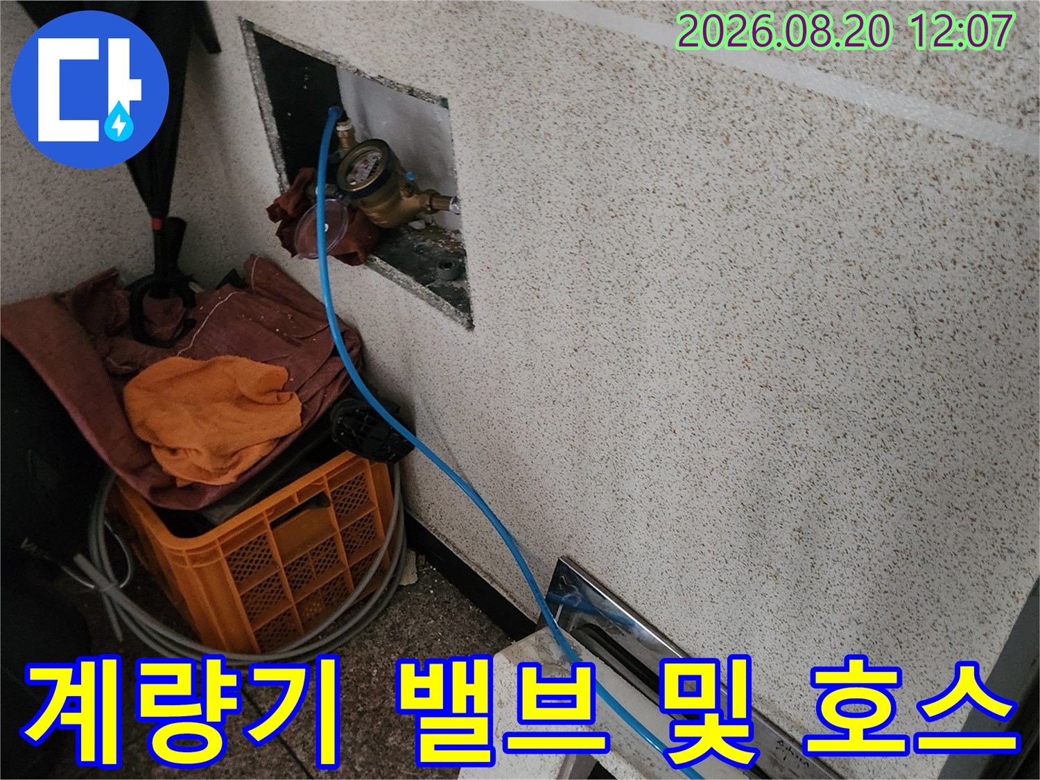 벽면 타일 사이에 설치된 수도 계량기와 파란색 점검선