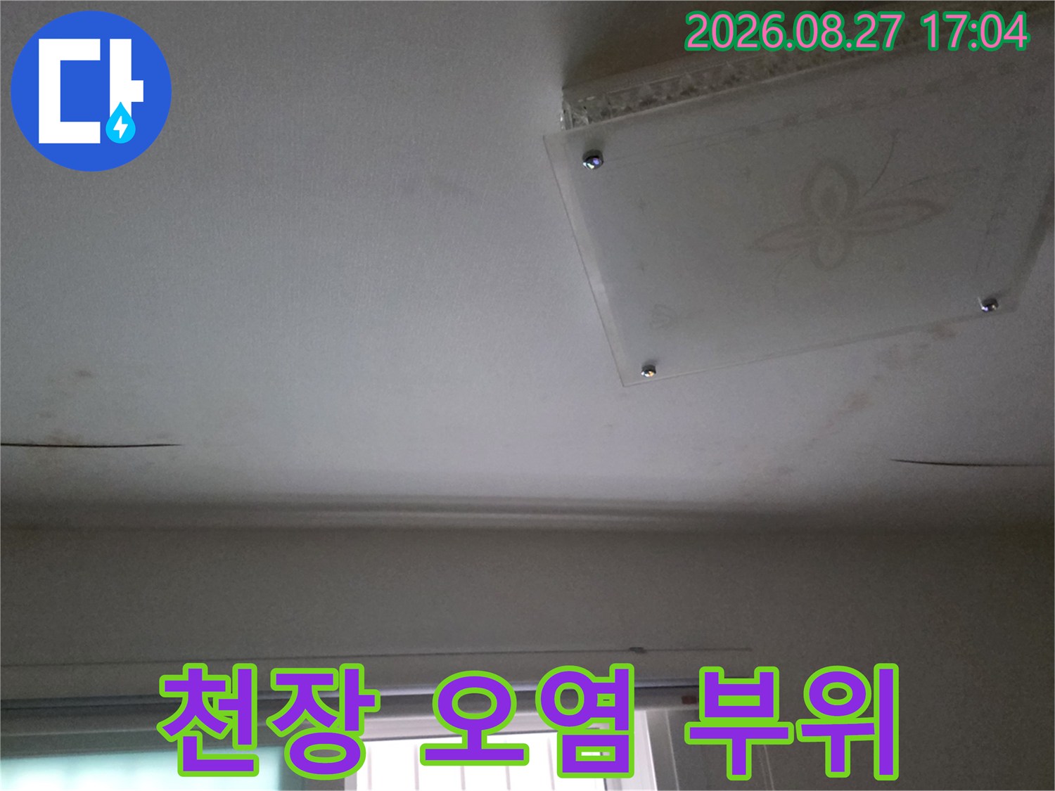 배관 누수로 인해 천장 점검구 주변에 발생한 어두운 얼룩과 습기 흔적입니다.