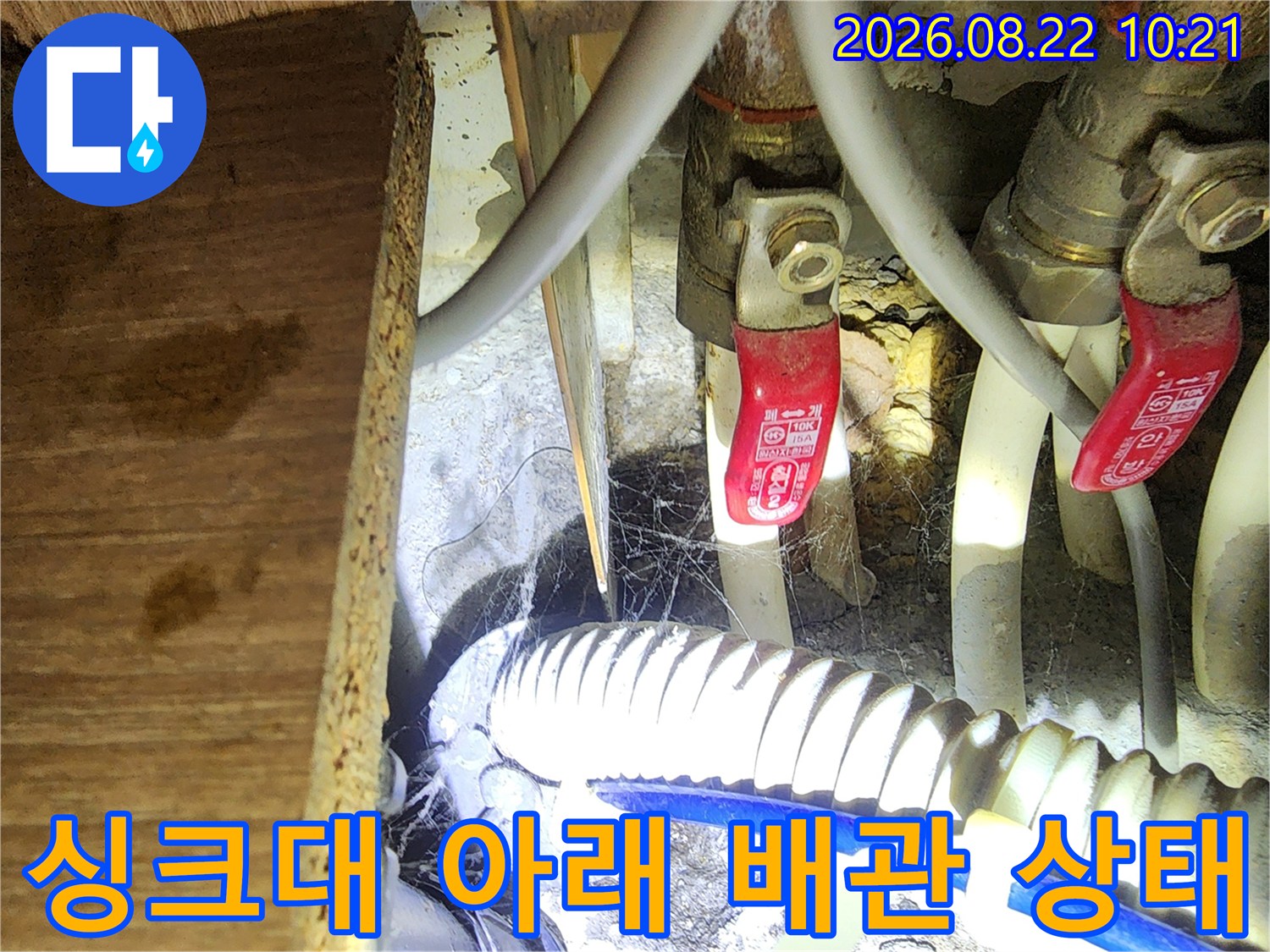 싱크대 하부장의 복잡한 배관 구조와 밸브 장치를 보여주는 사진입니다.