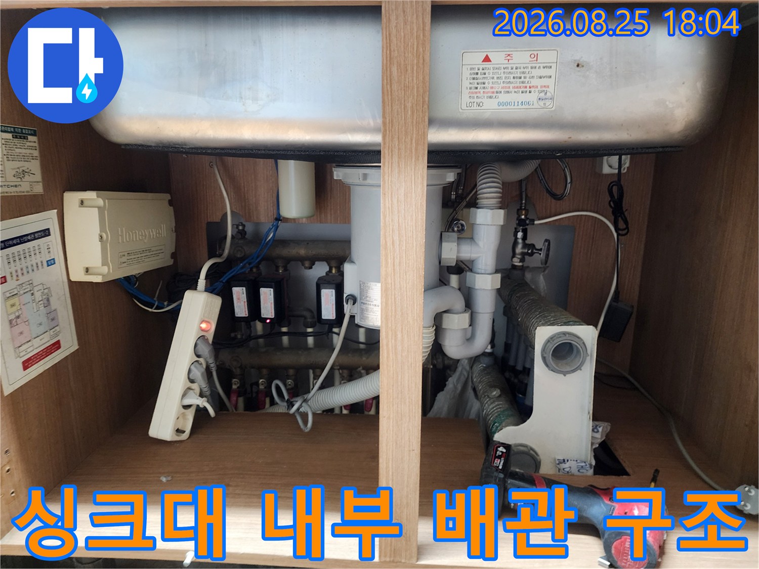 싱크대 하부 수납장 내부에 복잡하게 연결된 배수 및 전기 설비