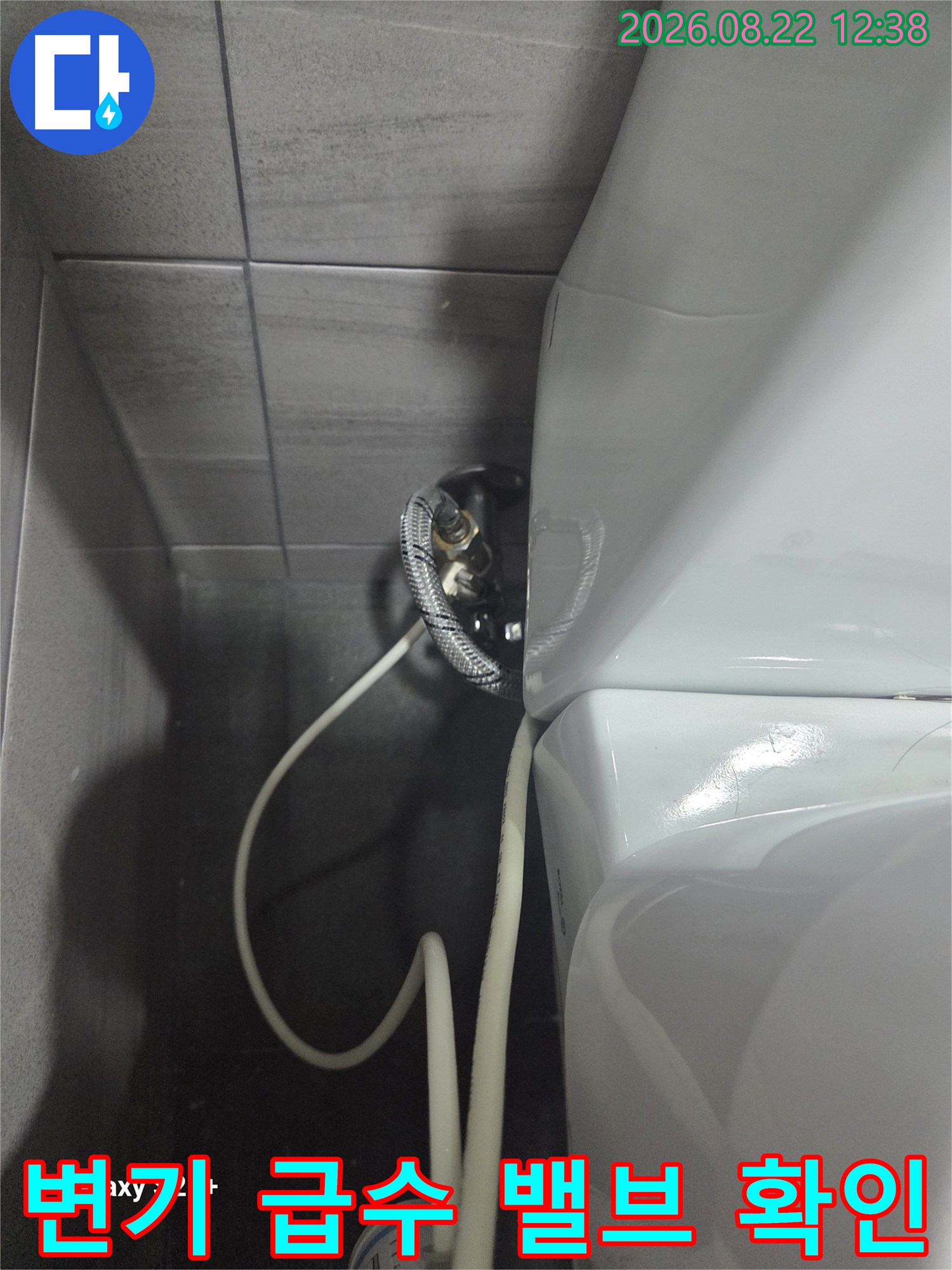 타일 벽면에 설치된 변기용 수도 밸브와 연결 호스입니다.