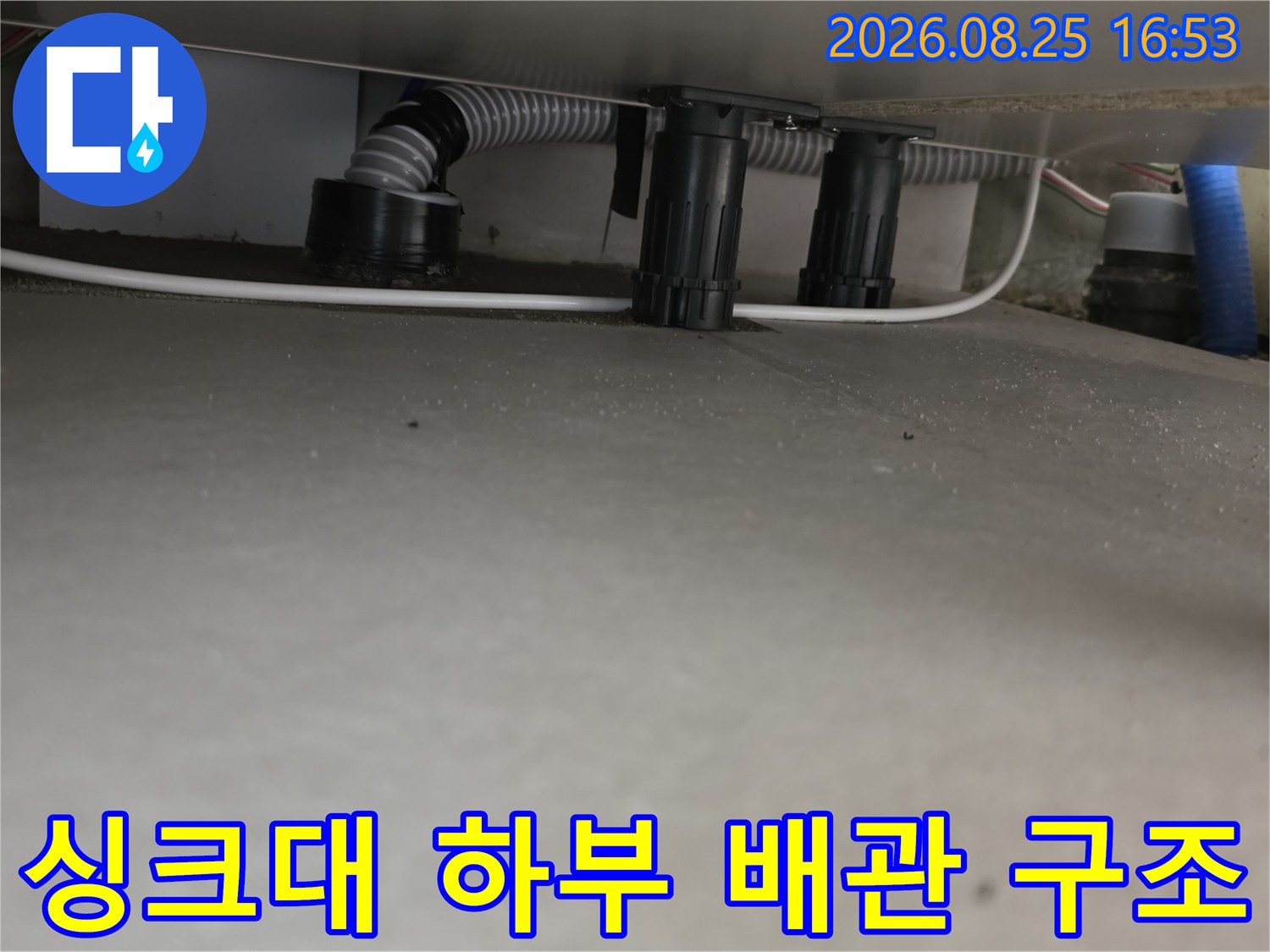 싱크대 아래쪽에 위치한 회색 주름관과 검은색 연결 소켓