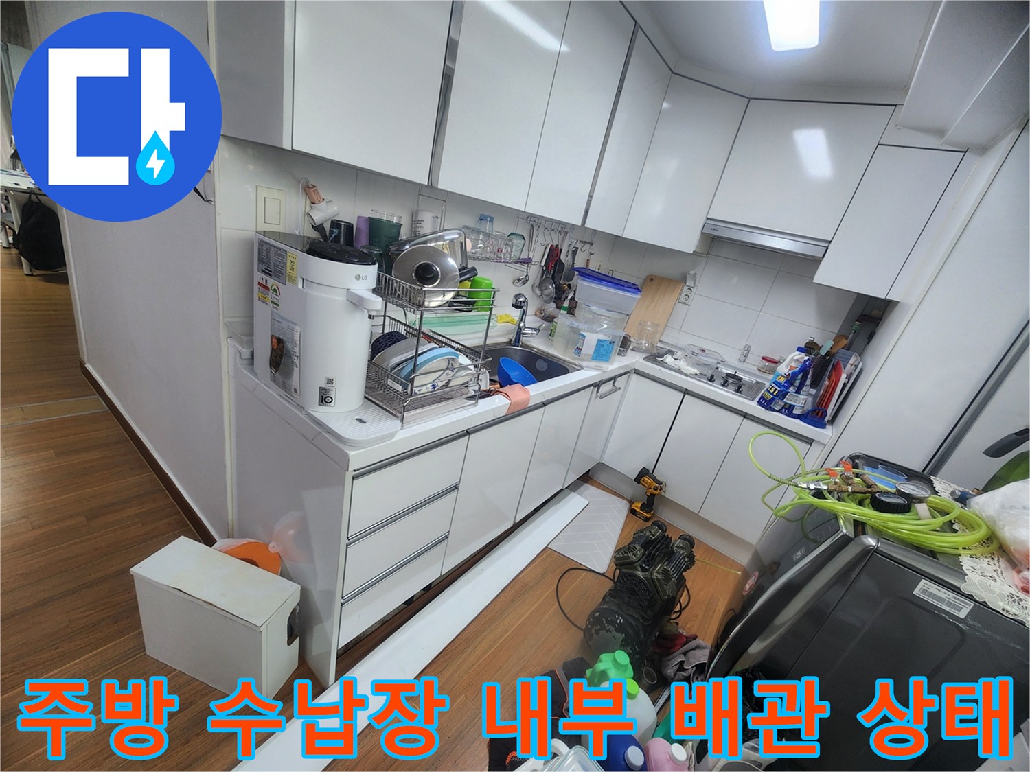 싱크대 하부장 안에 배치된 주방 용품과 배관 연결 부위 사진입니다.
