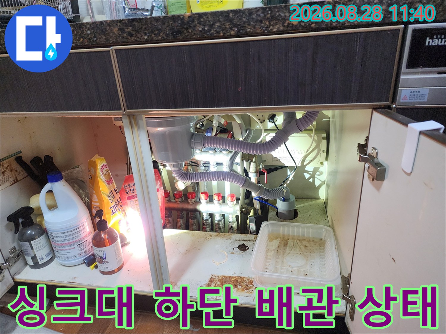 주방 싱크대 밑에 설치된 에어컨 드레인 호스와 복합적인 배관 연결 모습