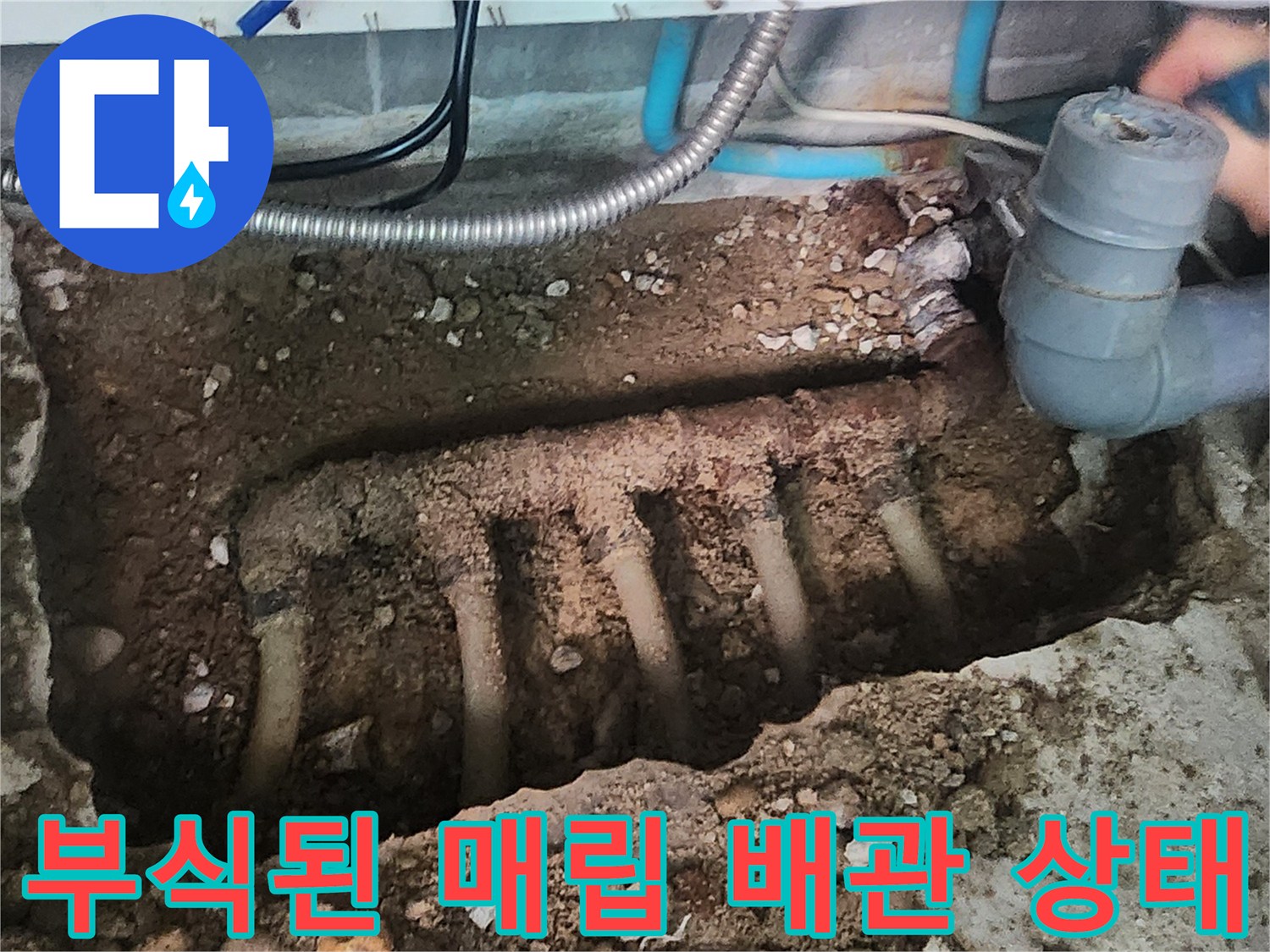 흙과 자갈 사이로 드러난 노후된 금속 분배기와 하수관 연결 부위