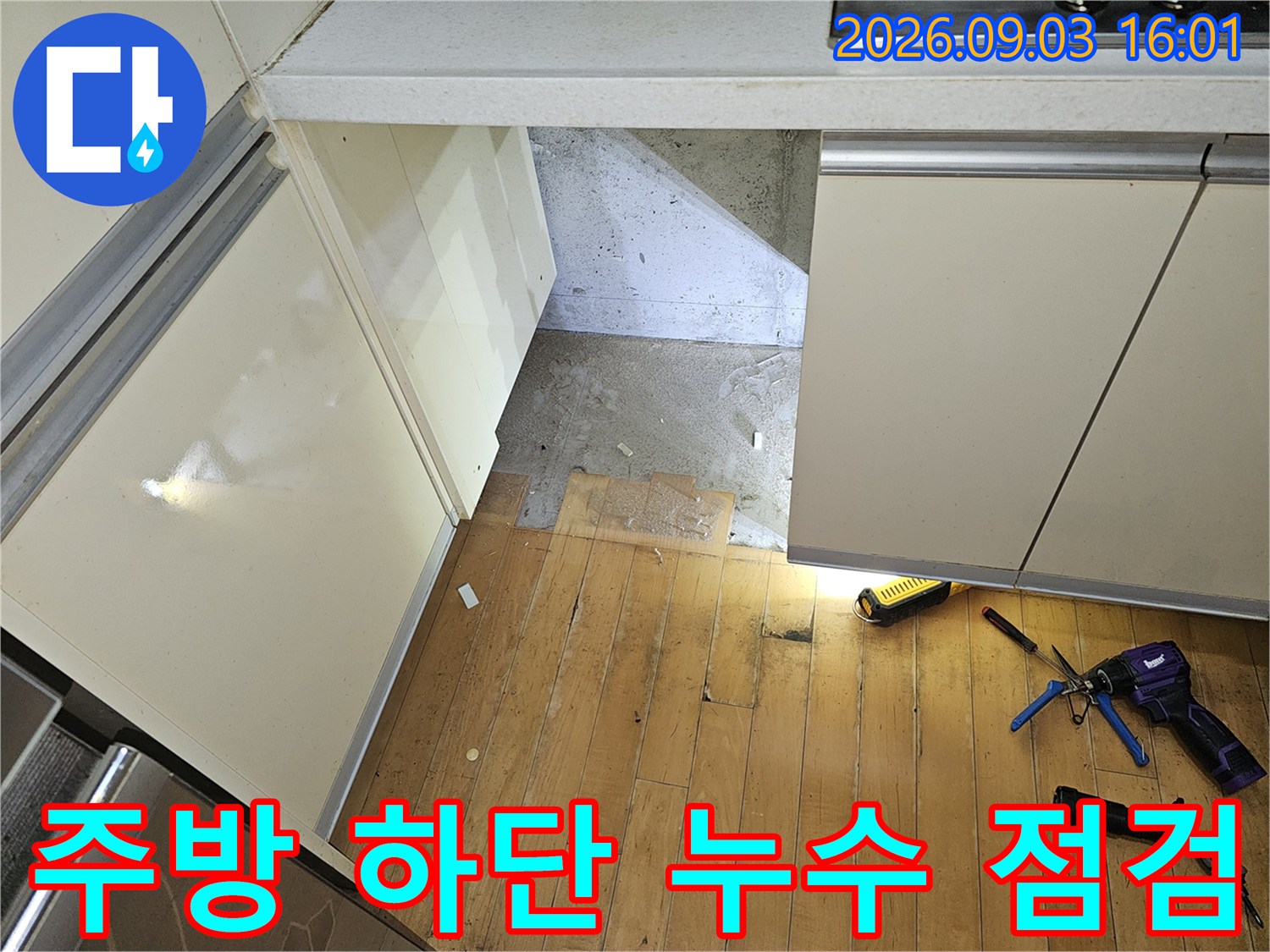 싱크대 아래 작업 공간에 랜턴과 공구를 두고 배관 상태를 살피는 모습입니다.