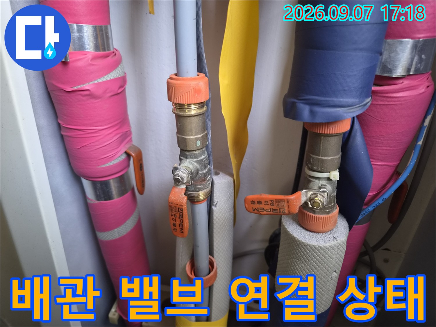 분홍색 보온재로 마감된-배관과 오렌지색 손잡이 밸브의 모습입니다.