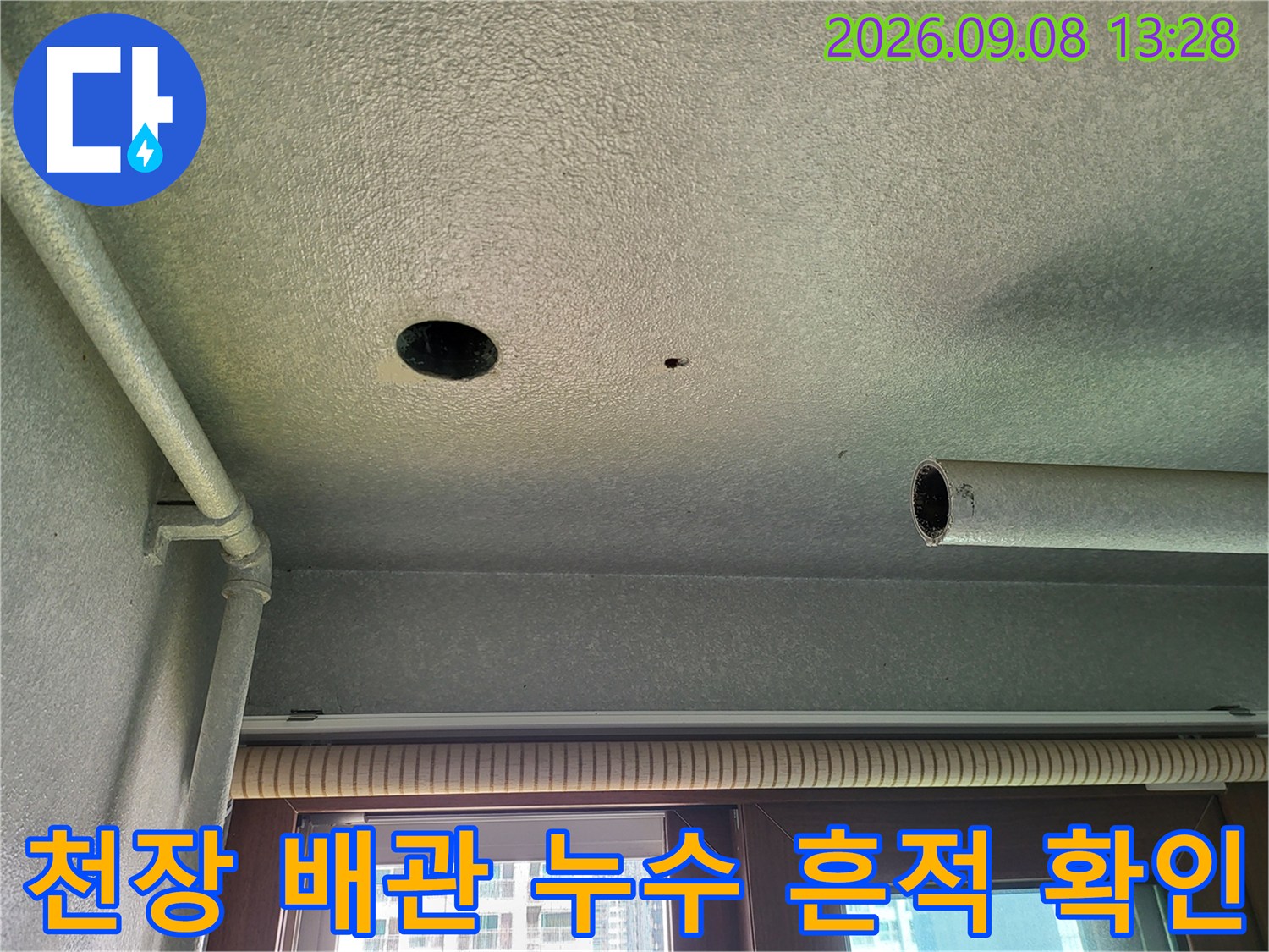 하얀색 천장 마감재에 설치된 굵은 배관과 작은 구멍을 촬영한 사진입니다.