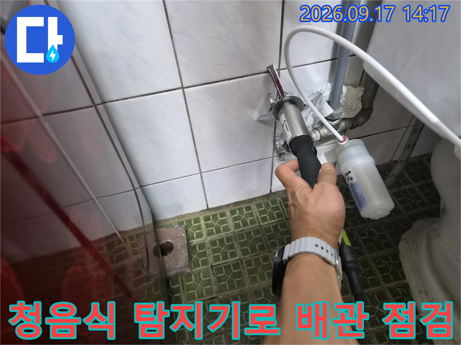 화장실 타일 벽면의 수도 배관 부근에서 청음식 탐지기를 사용하여 누수 지점을 찾는 모습입니다.